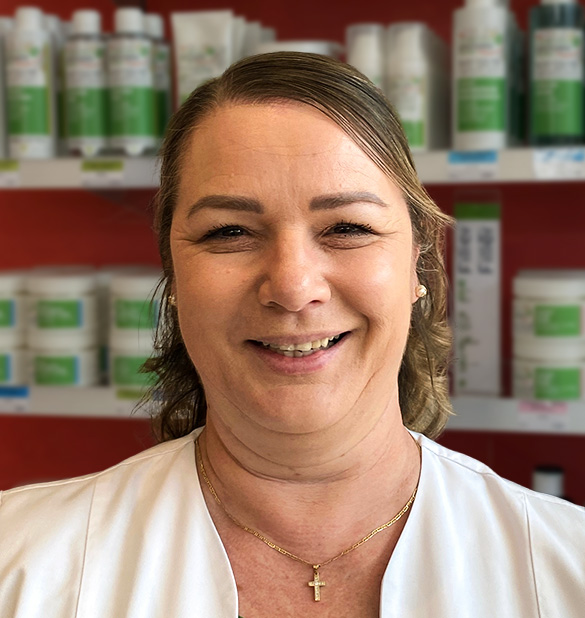 Eine Frau in einem weißen Kittel lächelt in den Regalen der Laurentius Apotheke Imst / Arzl im Pitztal.