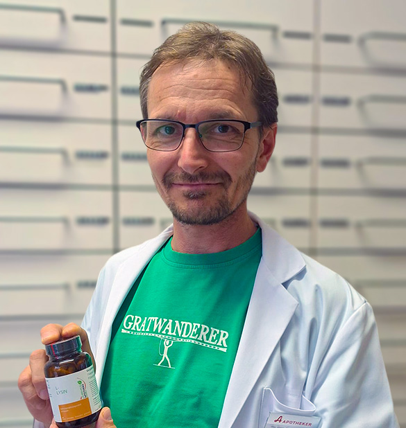 Ein Mann in einem weißen Kittel aus der Laurentius-Apotheke in Imst hält ein braunes Fläschchen vor einige Schubladen.