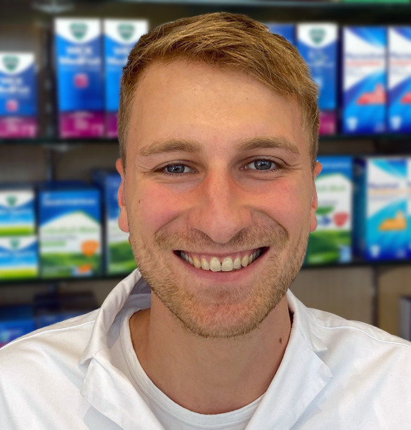 Eine lächelnde Person im Laborkittel vor den Regalen der Laurentius Apotheke Imst / Arzl im Pitztal.